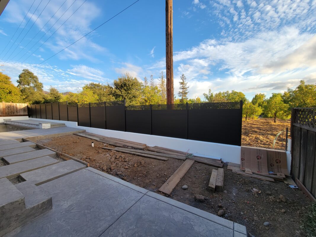 Modern black aluminum fence panels installed in a residential landscape under a blue sky.