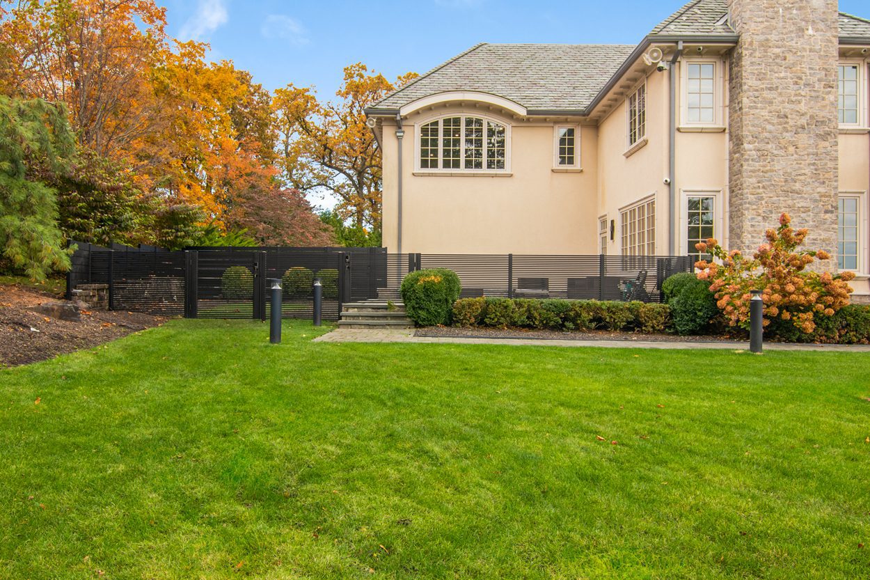 A modern black aluminum fence surrounds a lush green lawn and elegant home.