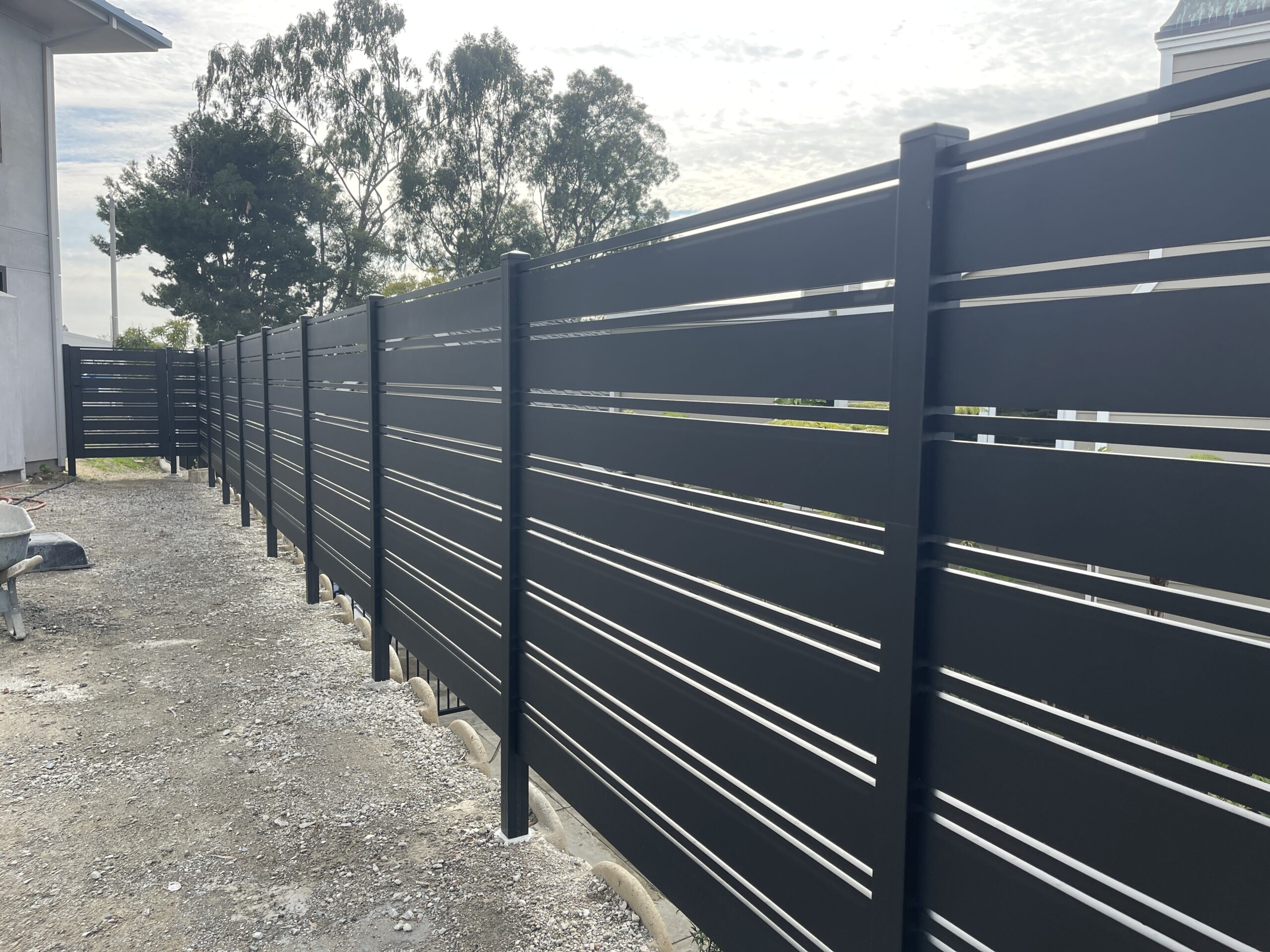 A sleek black aluminum fence installation in progress beside a pathway.