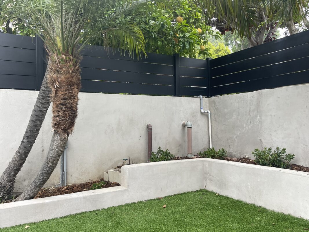 A modern black fence with a privacy wall, palm trees, and landscaped area.