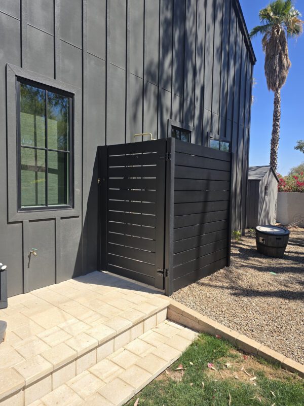 Aluminum privacy gate in satin black installed next to a modern home with landscaped yard.