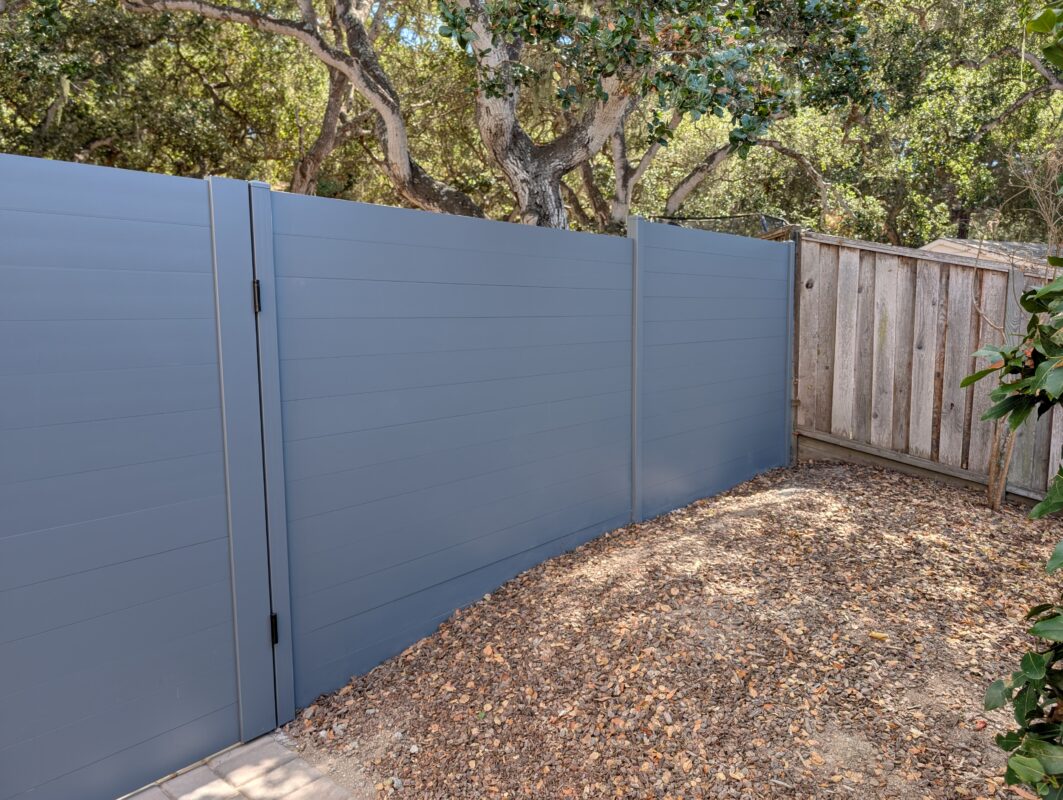 A newly installed light gray aluminum fence in a landscaped yard.