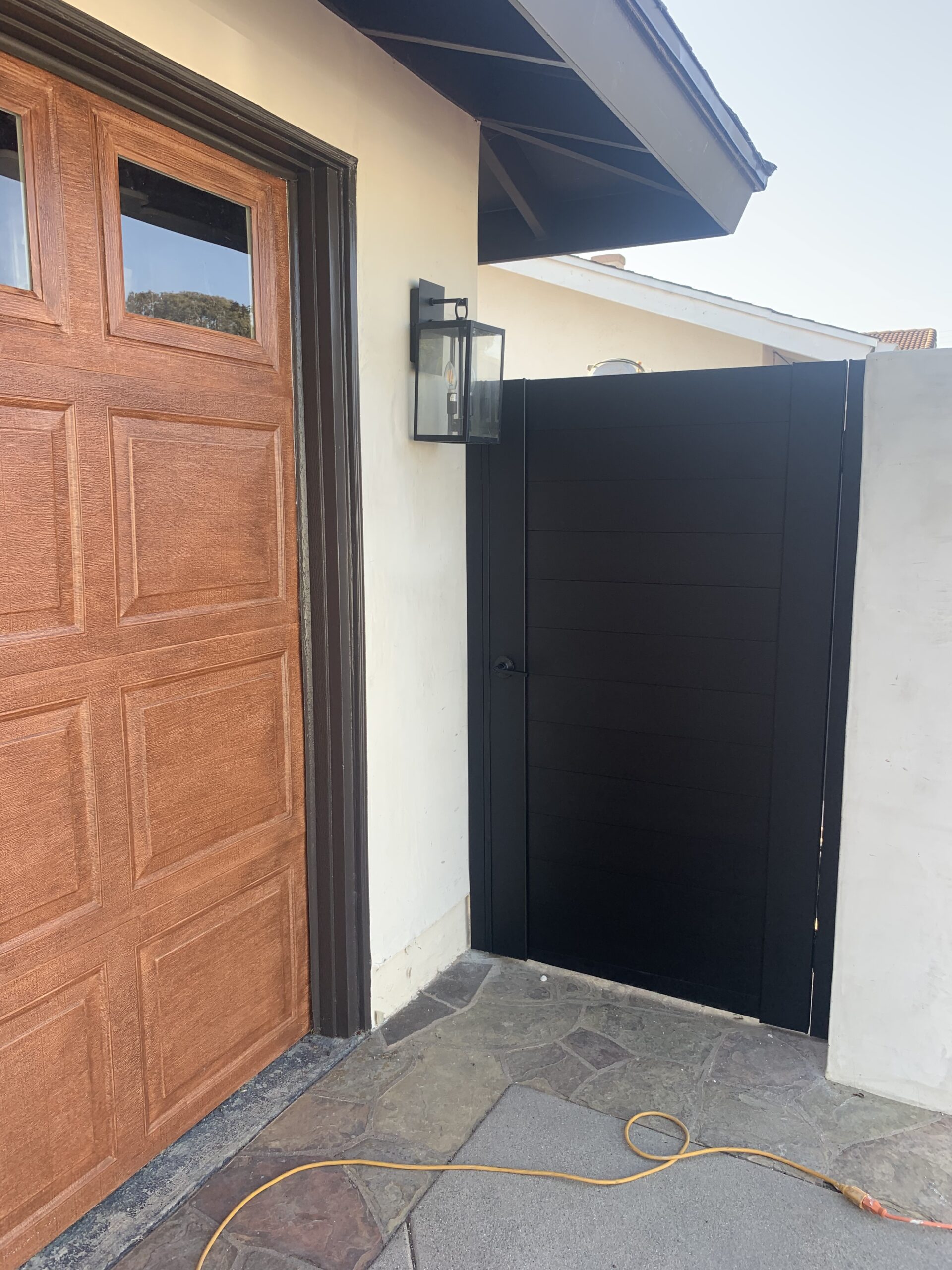 A modern matte black aluminum gate next to a wooden door, enhancing property privacy.
