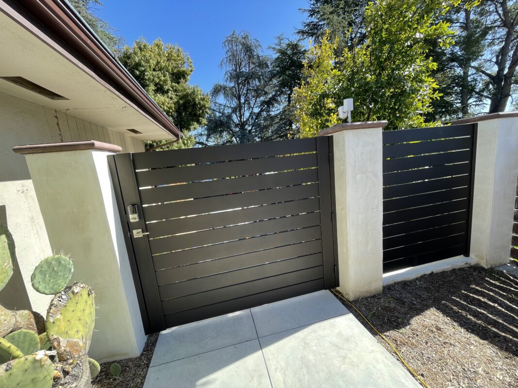 Modern bronze aluminum side yard gate installation amidst greenery and a clear blue sky.