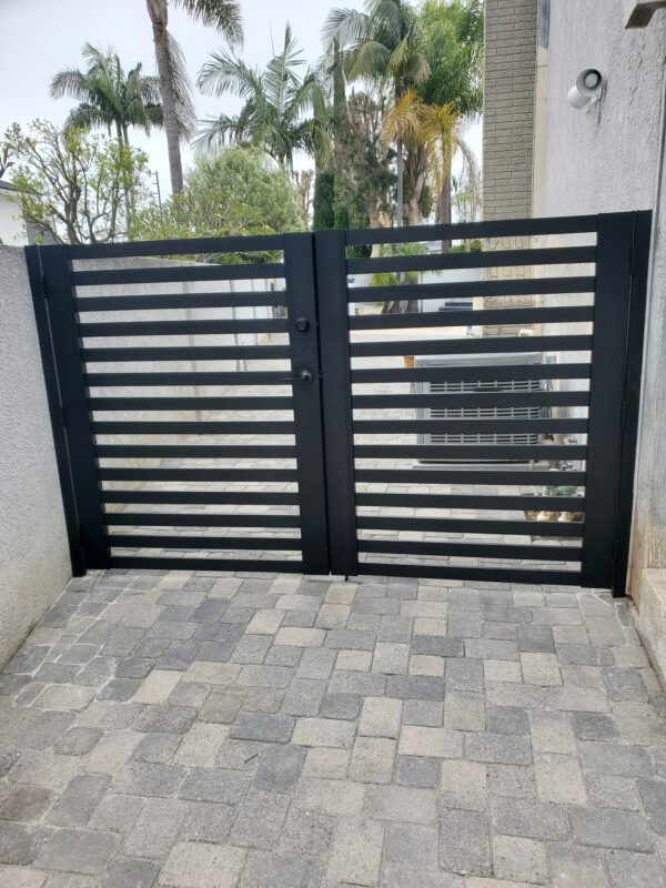 Black aluminum double swing gate installed in a modern residential setting with landscaping.