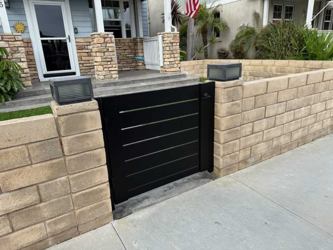 Matte black aluminum gate installation with stone wall and light fixtures.