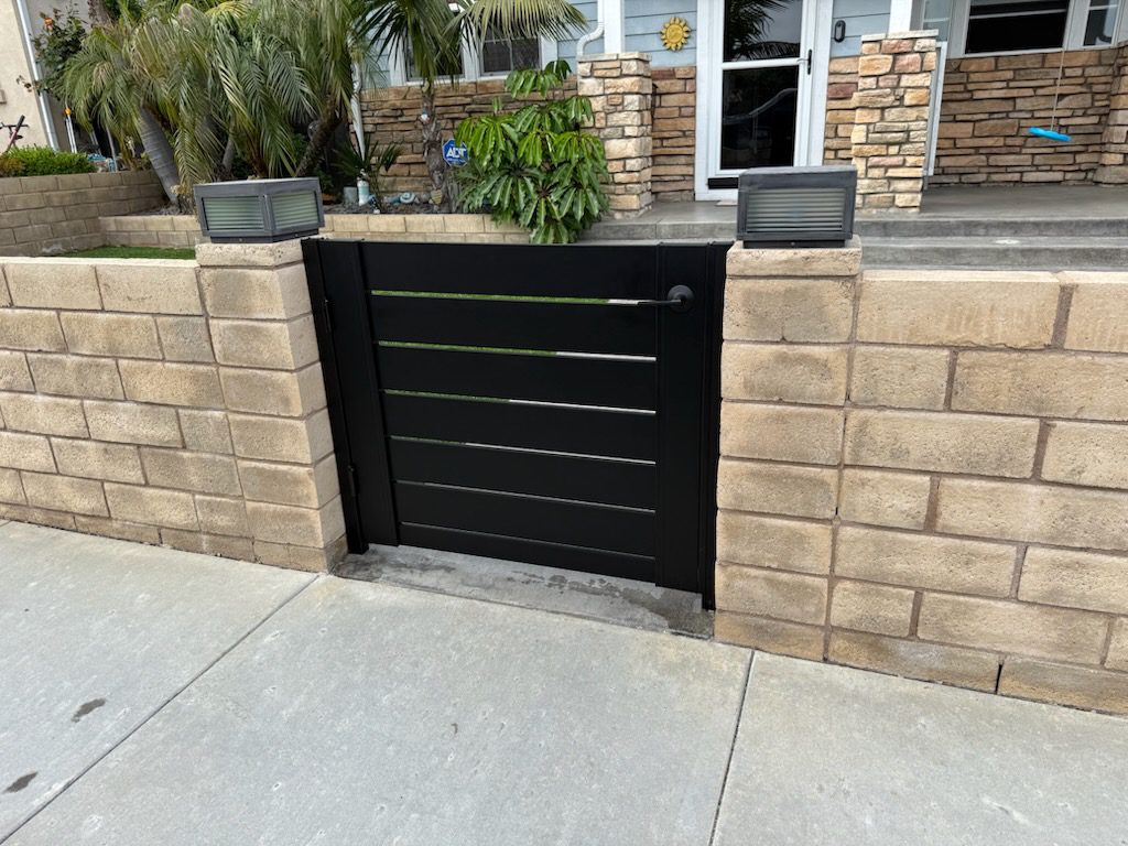 Matte black aluminum gate installed between stone walls, enhancing entryway privacy.