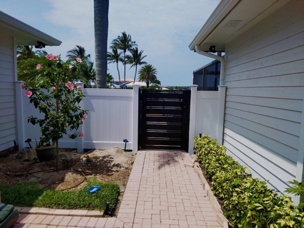 Modern matte black aluminum gate between white fences and landscaping in sunny Vero Beach.
