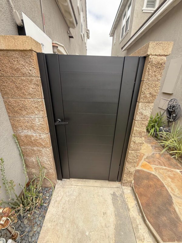 Matte black aluminum gate with stone pillars, offering full privacy in Tustin, CA.
