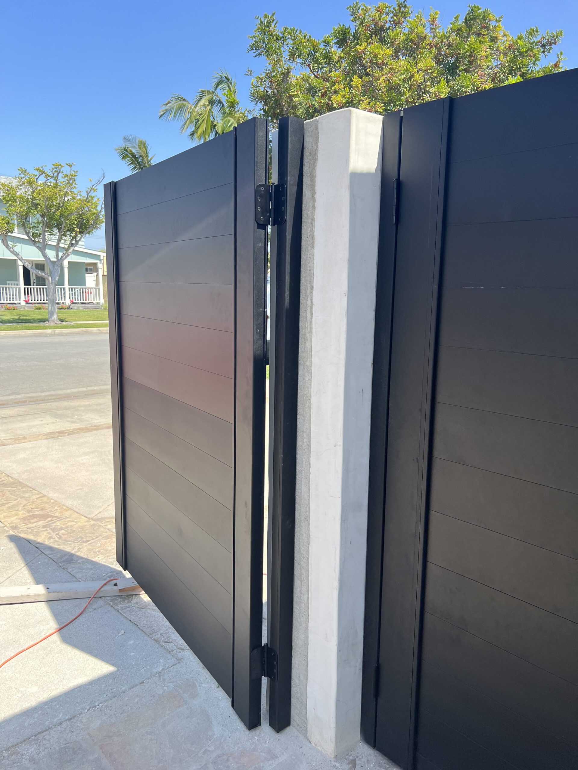 Close-up of a matte black aluminum gate, partially open near a concrete post.
