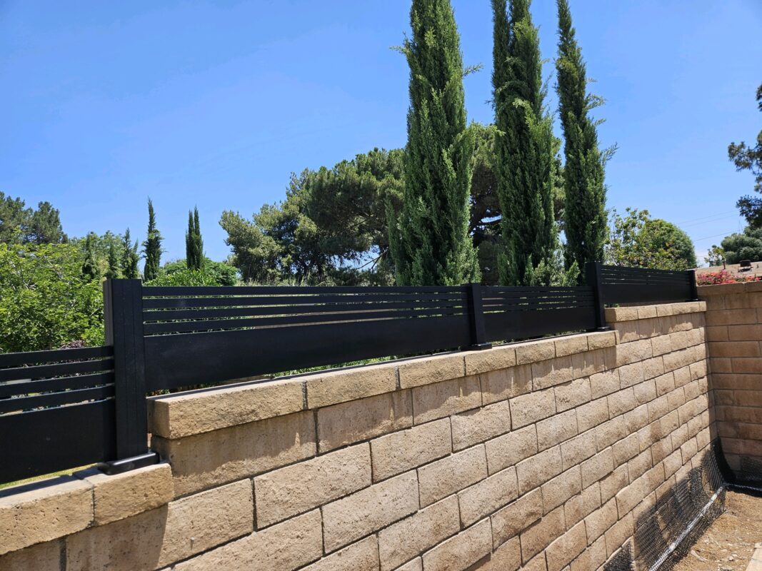 Matte black aluminum wall topper with horizontal slats on top of a stone fence.
