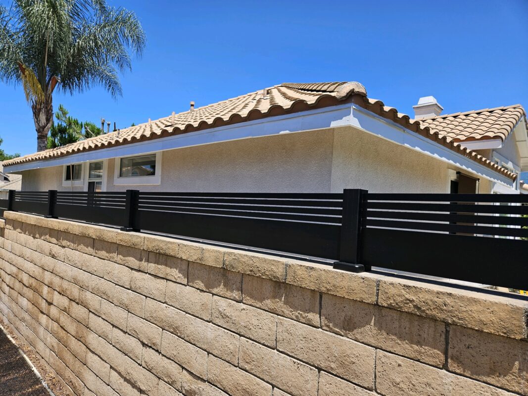 Black aluminum fence atop a stone wall, enhancing privacy for a residential property.