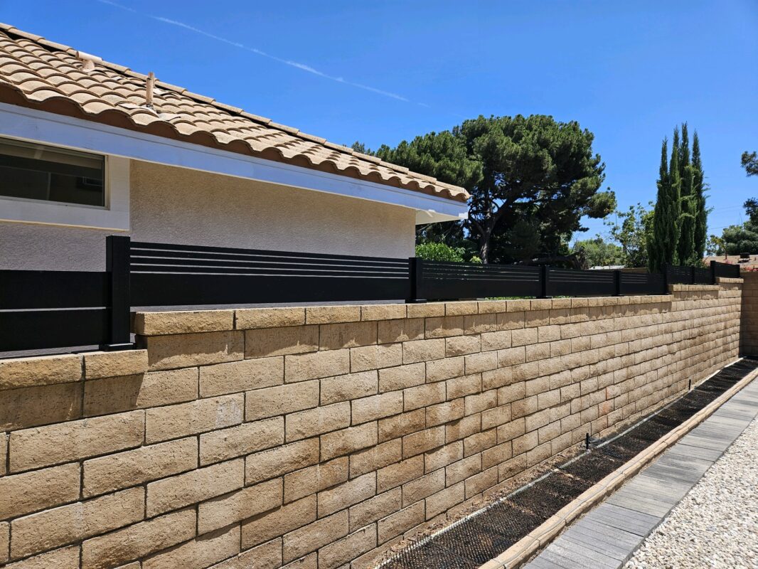 Black aluminum wall topper and gates on a stacked stone wall in a bright outdoor setting.
