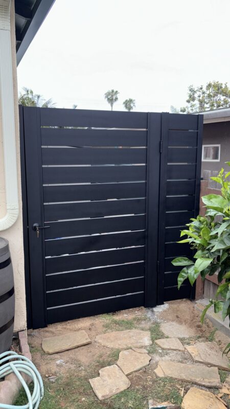 Matte black aluminum gate with horizontal slats installed in a backyard setting.