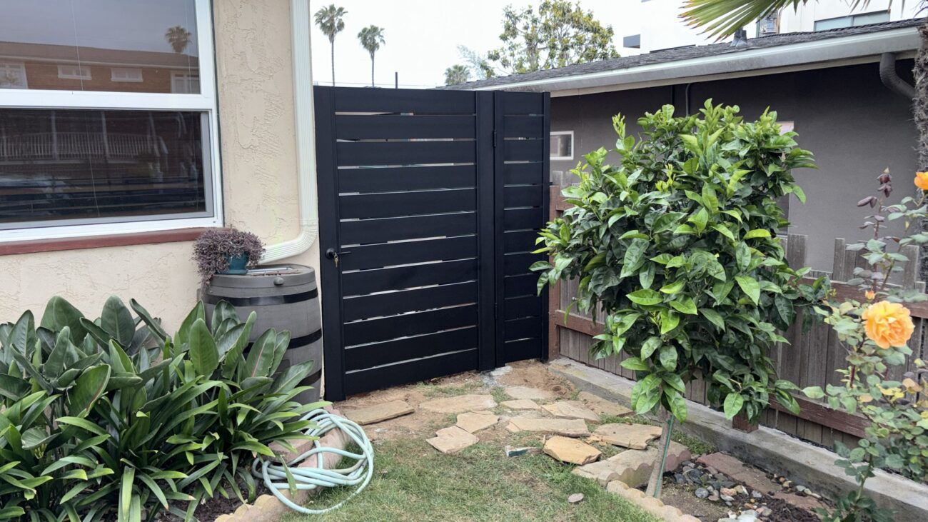 Matte black aluminum gate with horizontal slats, surrounded by lush greenery.