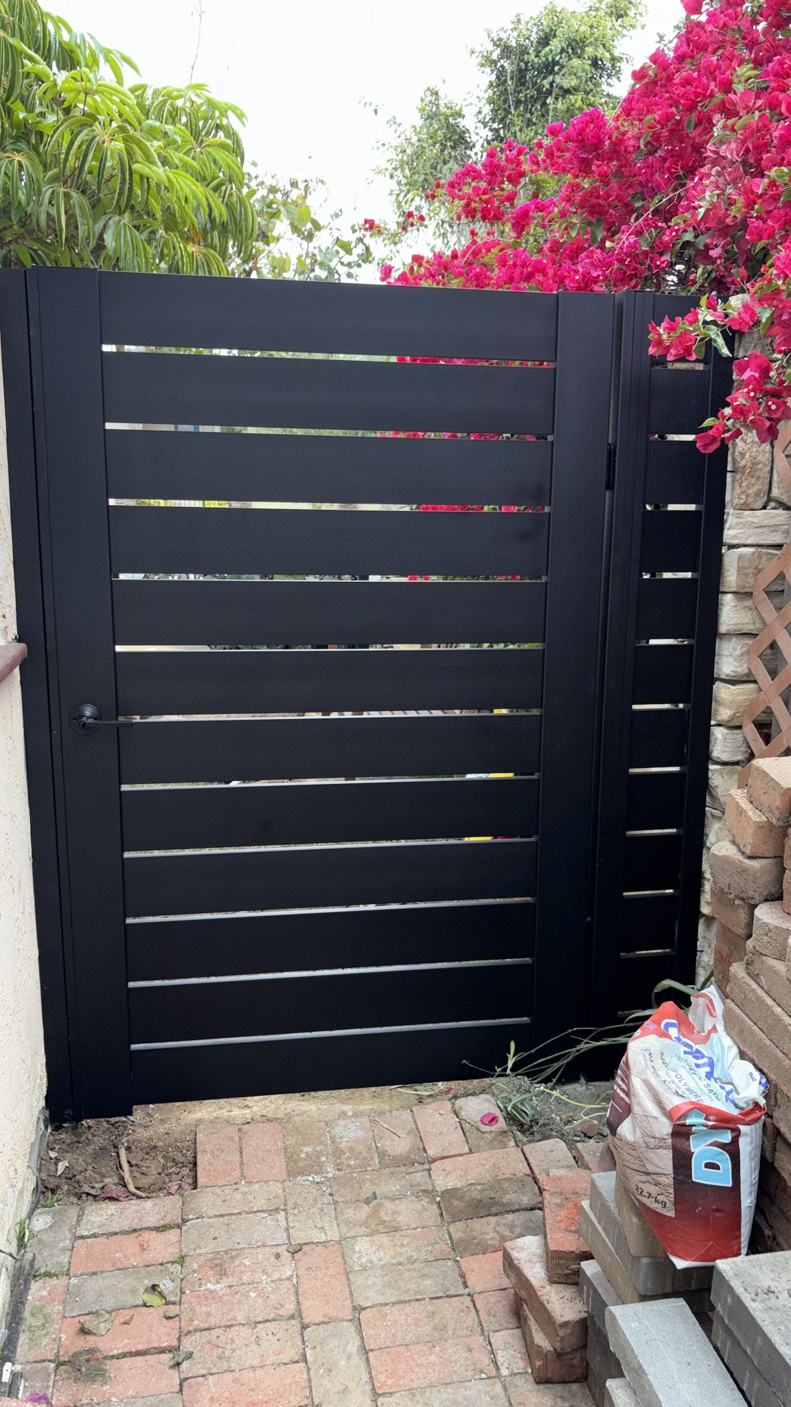 Matte black aluminum gate with horizontal slats, surrounded by vibrant flowers.