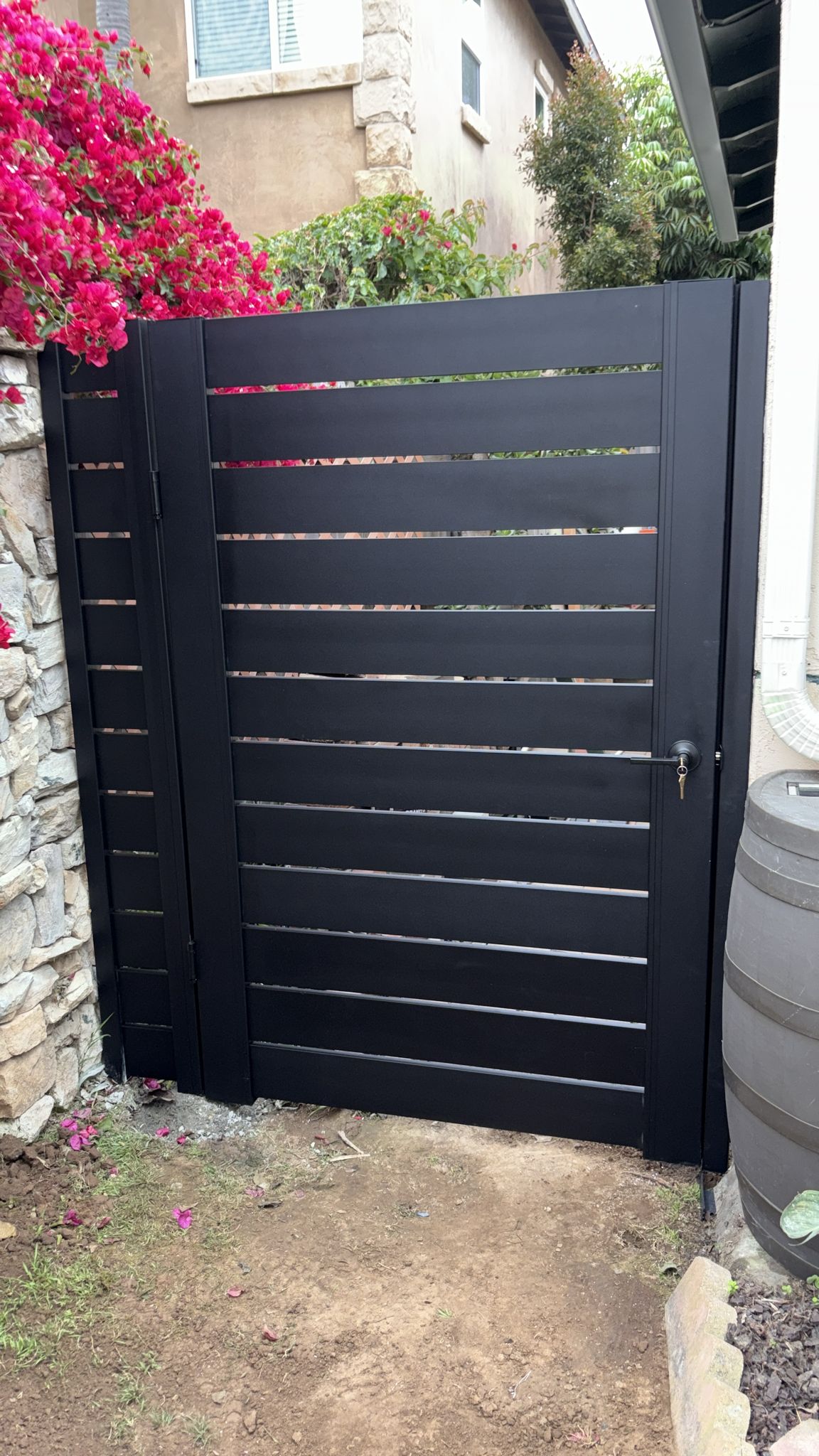 Matte black aluminum gate with horizontal slats, surrounded by bougainvillea flowers.