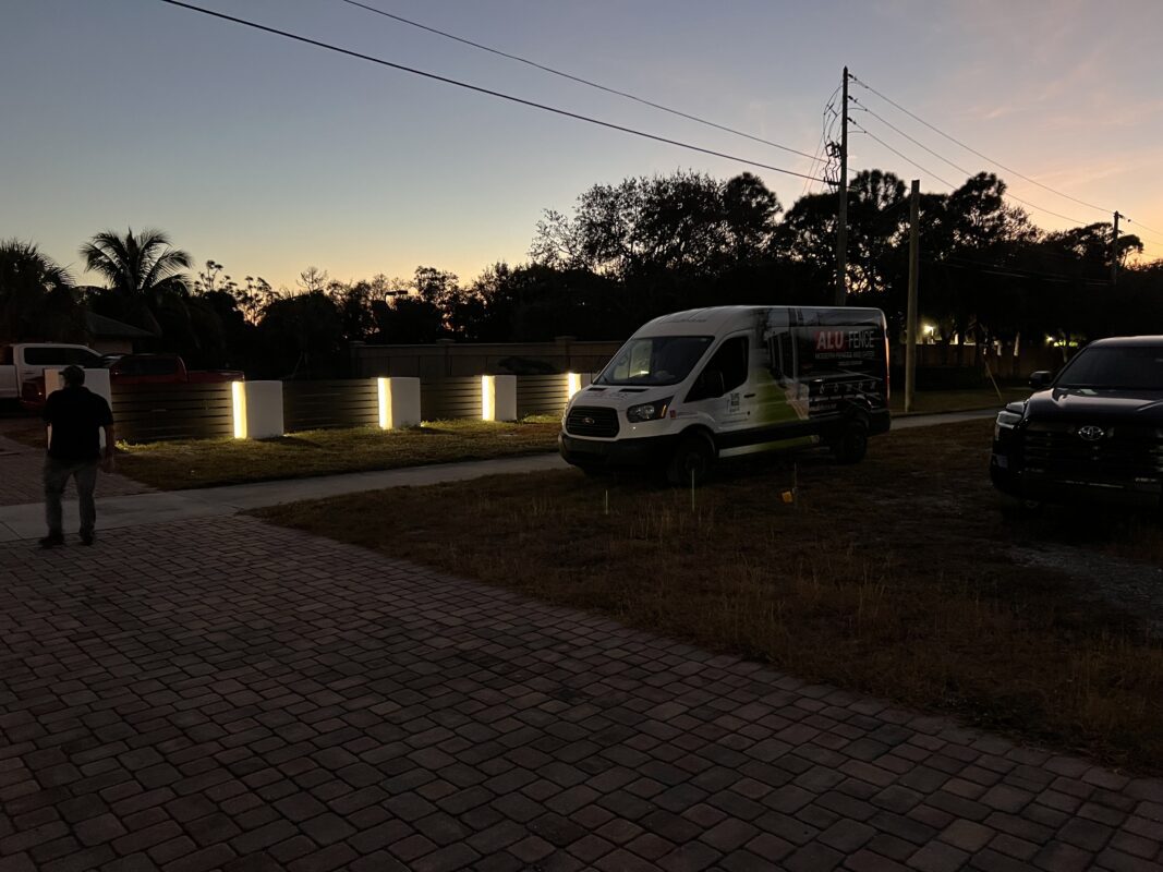 A person walks near a modern aluminum fence with built-in lights at dusk in Jupiter, FL.