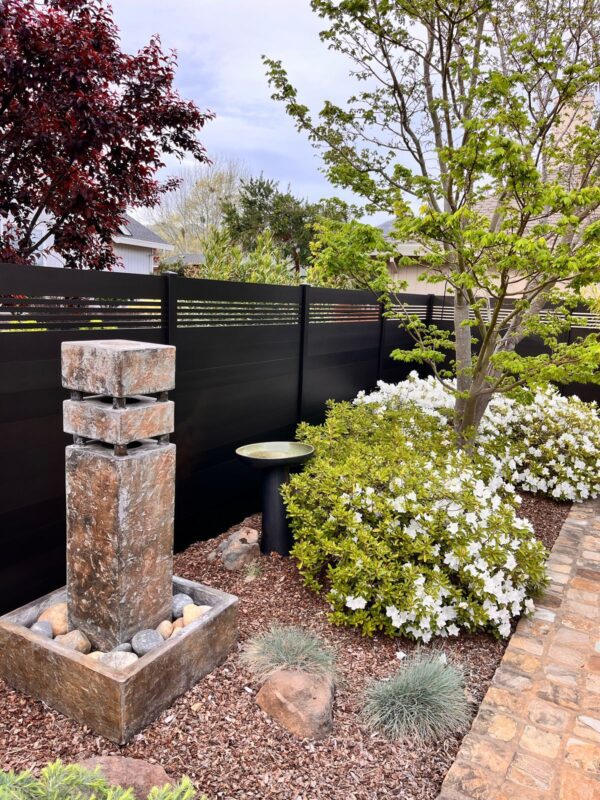 A modern black aluminum fence surrounds a landscaped garden with flowers and stone features.
