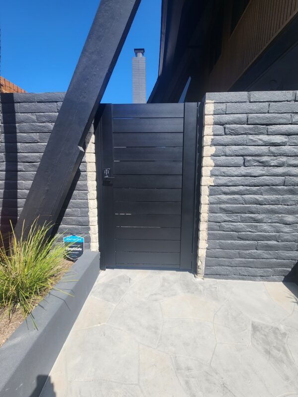 Matte black aluminum gate and wall topper with horizontal slats in a modern setting.