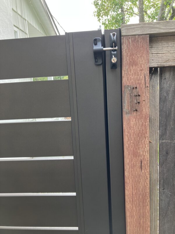 Close-up of a dark bronze aluminum pedestrian gate with horizontal slats and lock.