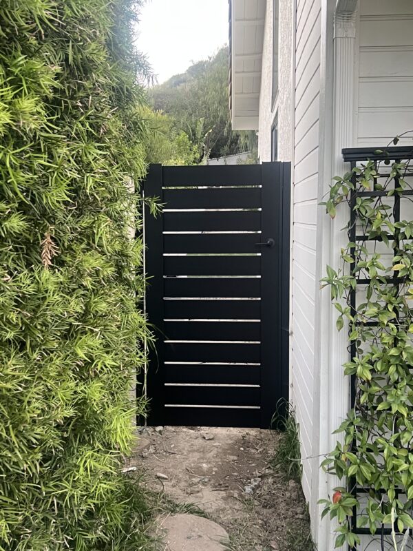 Black aluminum gate with horizontal slats in a garden pathway in Granada Hills, CA.