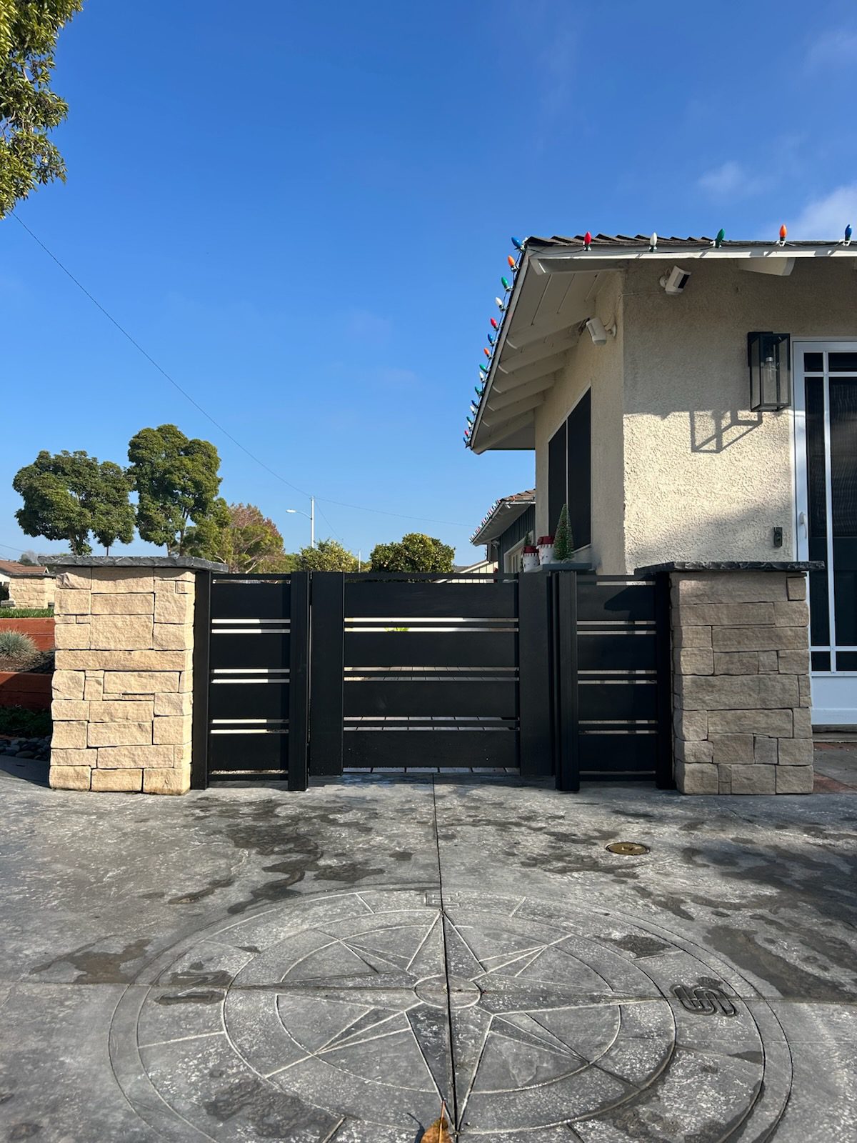 Modern black aluminum gate with stone pillars in a residential setting in Ventura, CA.