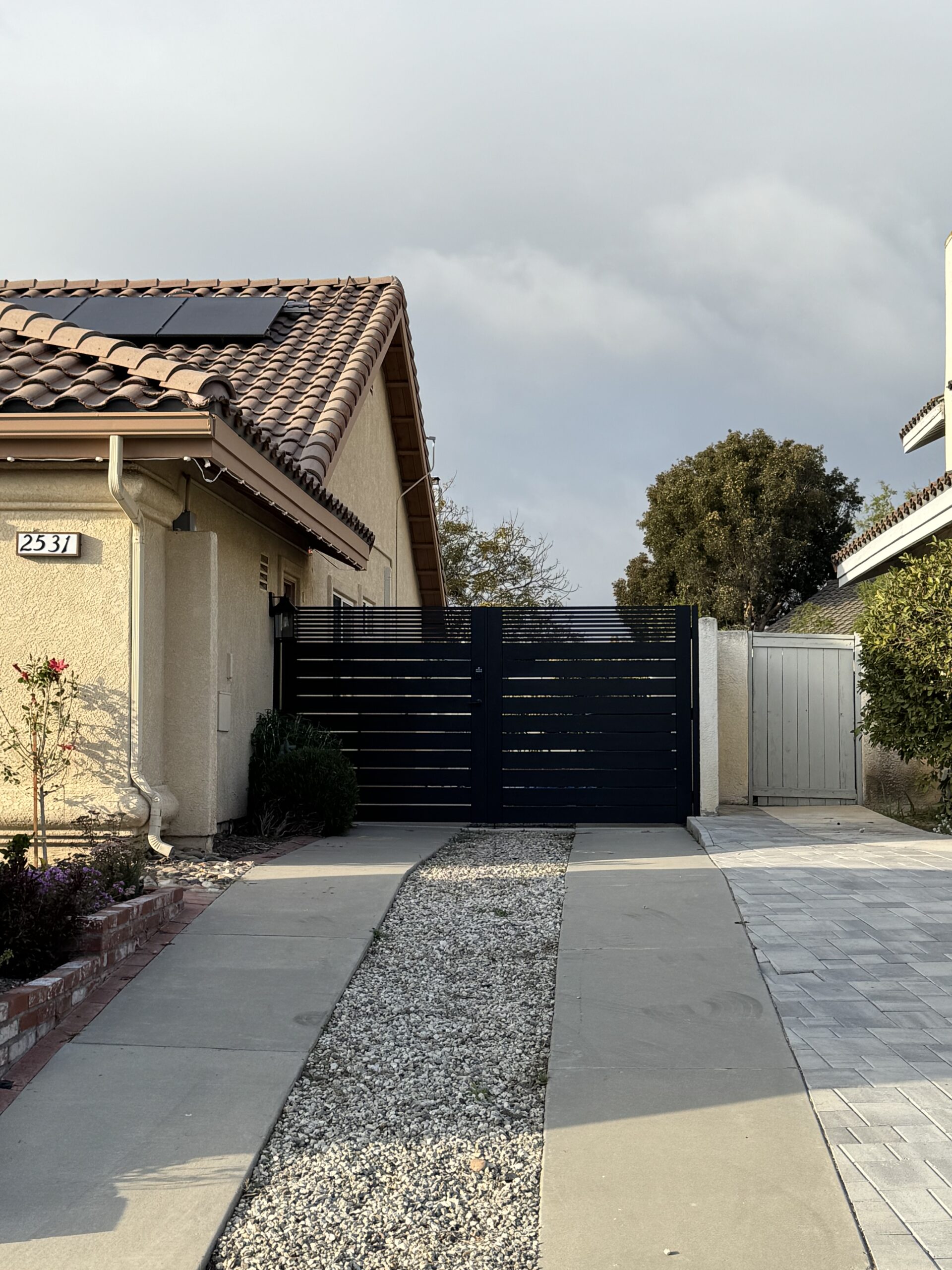 Matte black aluminum double swing gate with horizontal slats at a residential driveway.