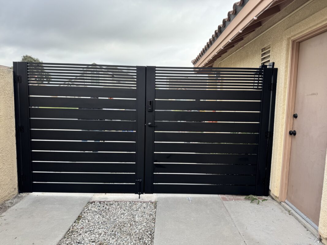 Matte black aluminum double swing gate with horizontal slats in a residential setting.