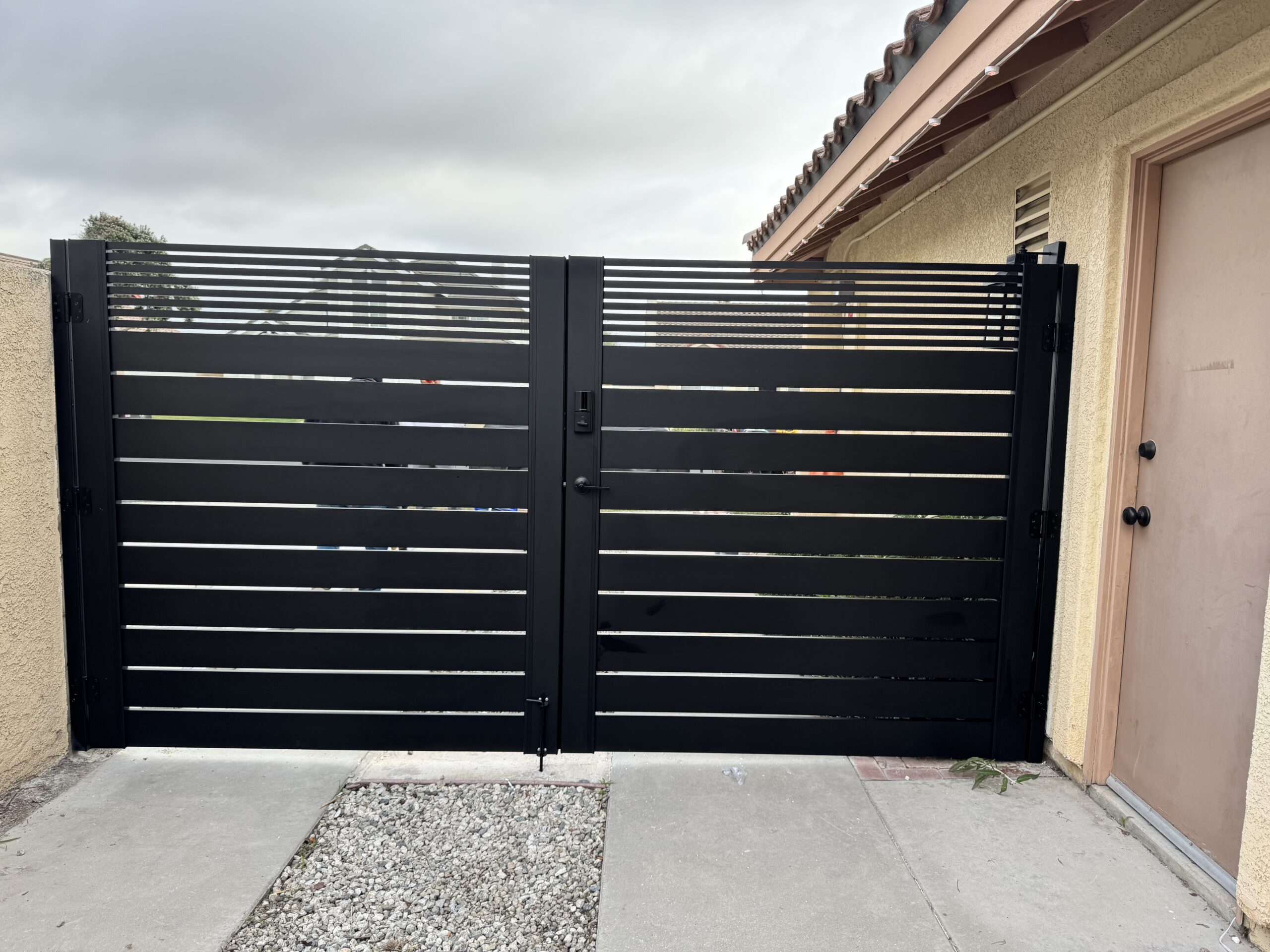 Matte black aluminum double swing gate with horizontal slats in a residential setting.