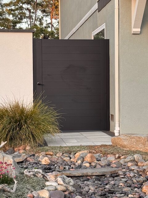 Matte black aluminum gate installation in a landscaped area with stones and plants.