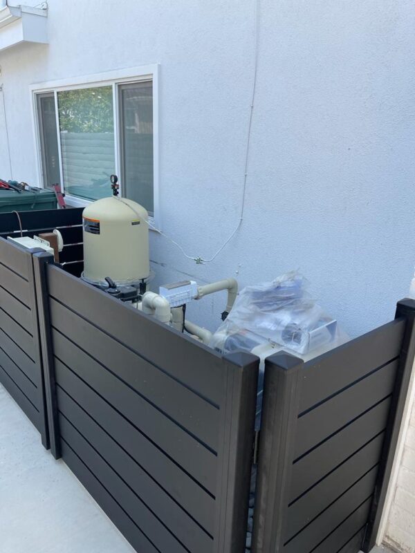 Black aluminum fence enclosing pool equipment next to a white wall in a residential area.