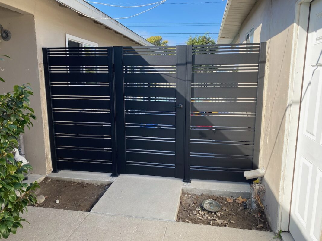 A sleek black aluminum slat pedestrian gate in a residential side yard.