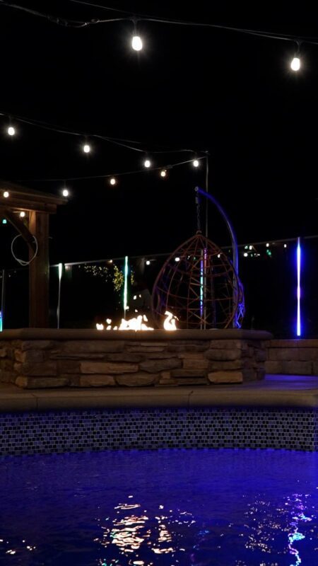 Nighttime outdoor scene with a stone fire pit, LED lights, and a hanging chair.