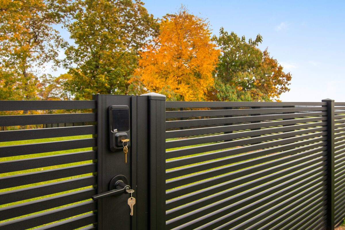 Modern black aluminum fence installation with a key and lush autumn foliage in background.