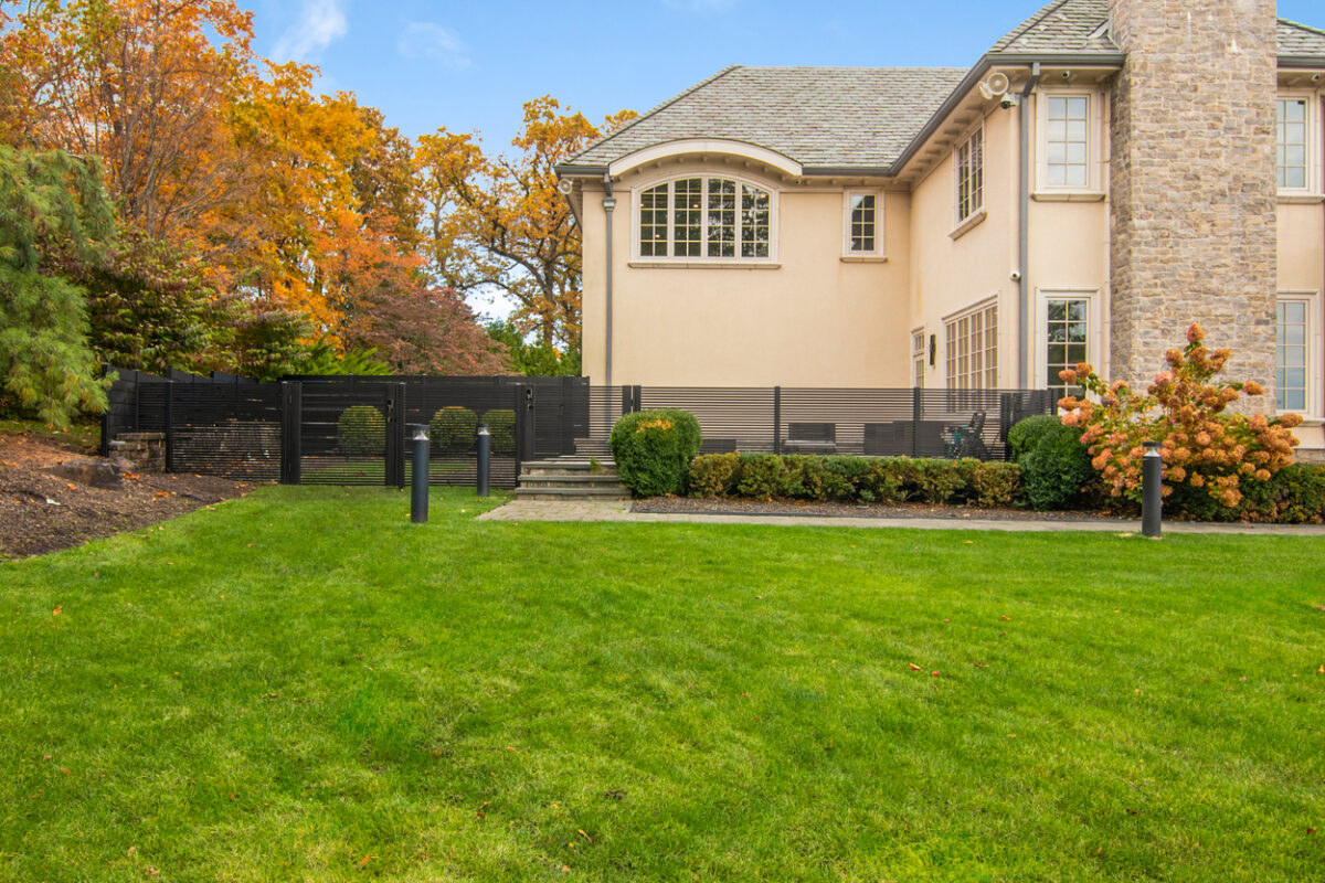 A modern black aluminum fence surrounds a lush green lawn and elegant home.