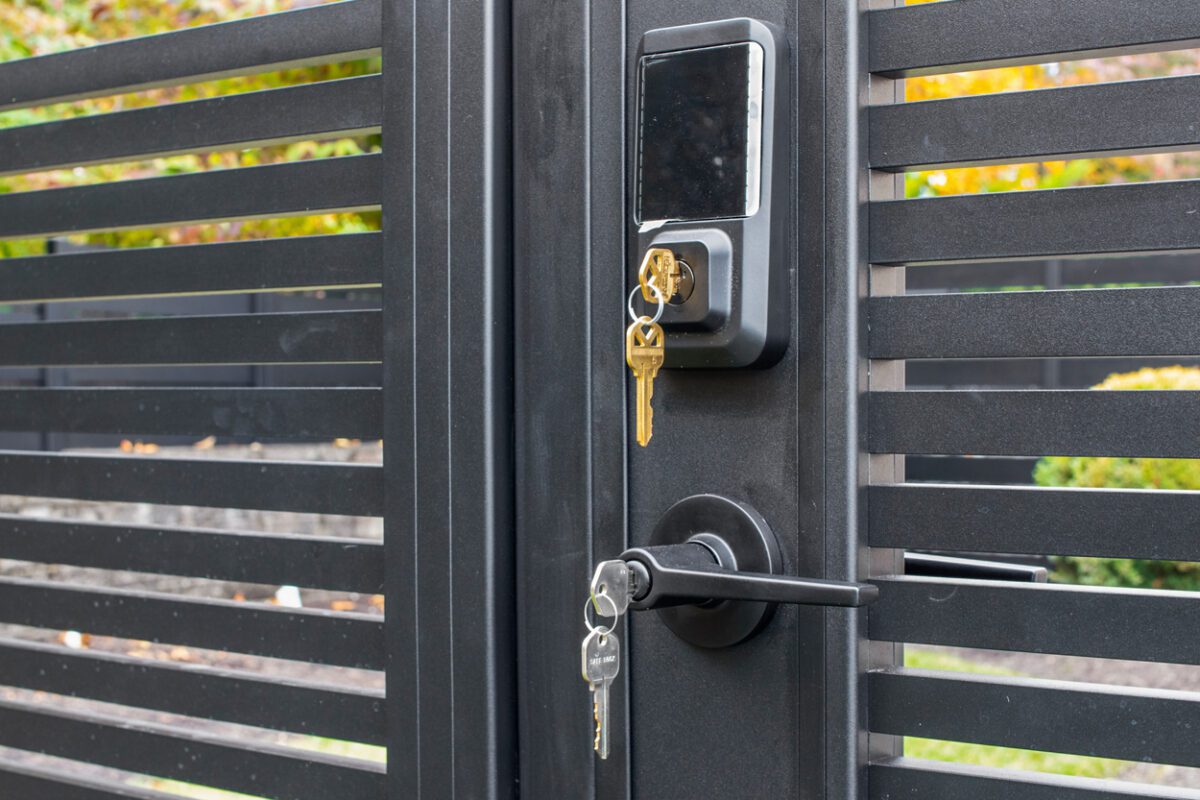 Close-up of a modern black aluminum fence gate with keys and lock.