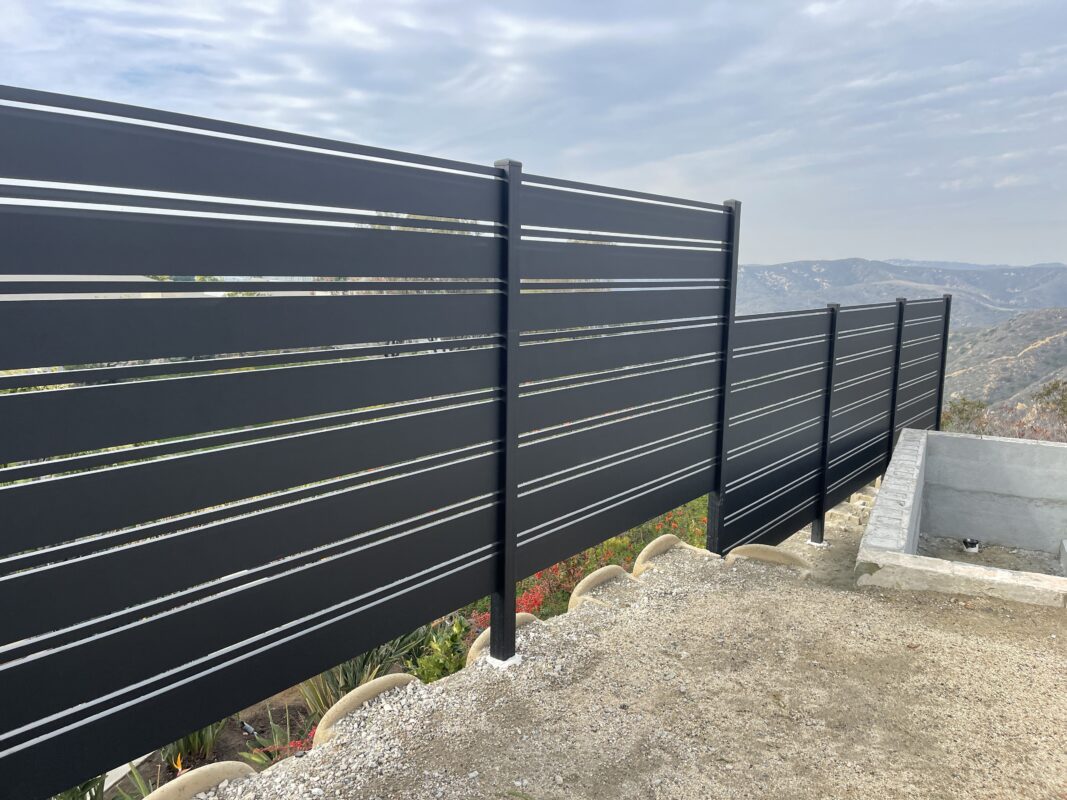 A newly installed black aluminum fence with horizontal slats, overlooking a mountainous landscape.