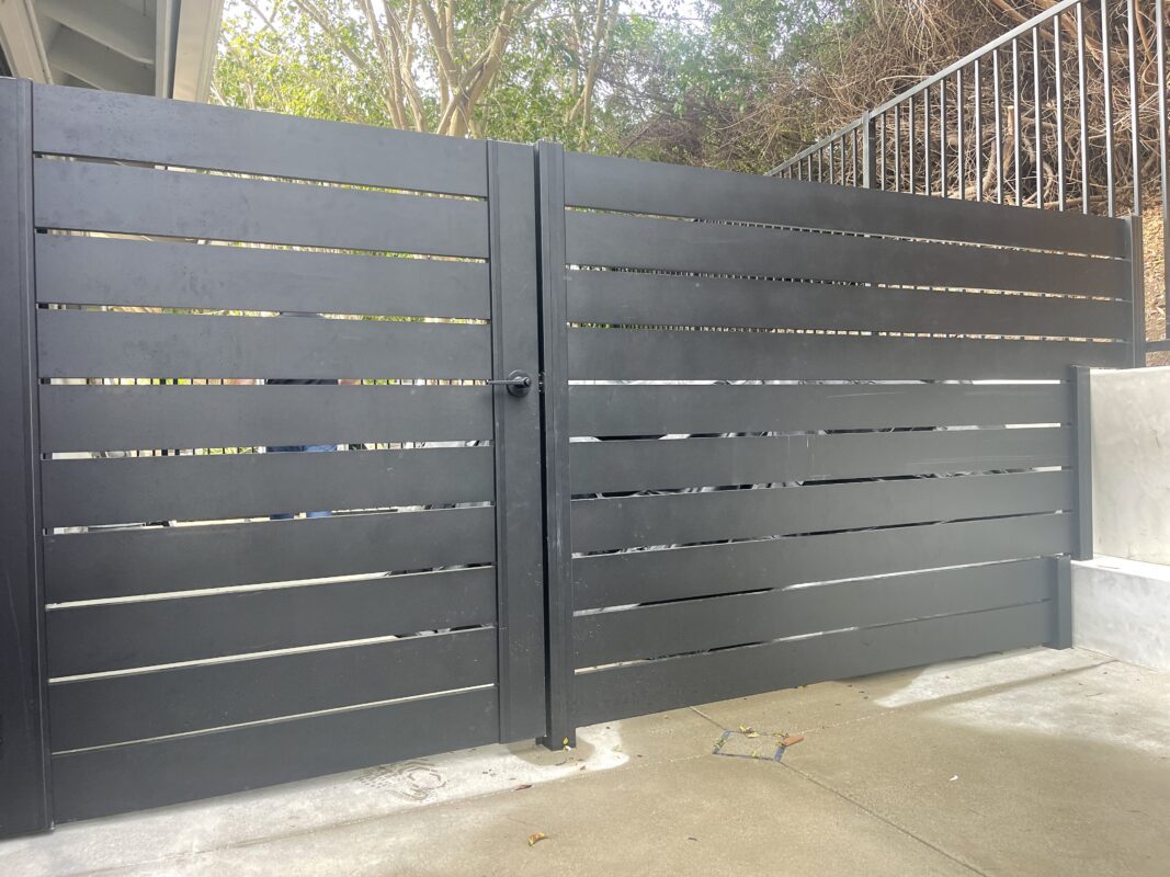 Modern black aluminum fence gate installed, blending style and durability in a patio area.
