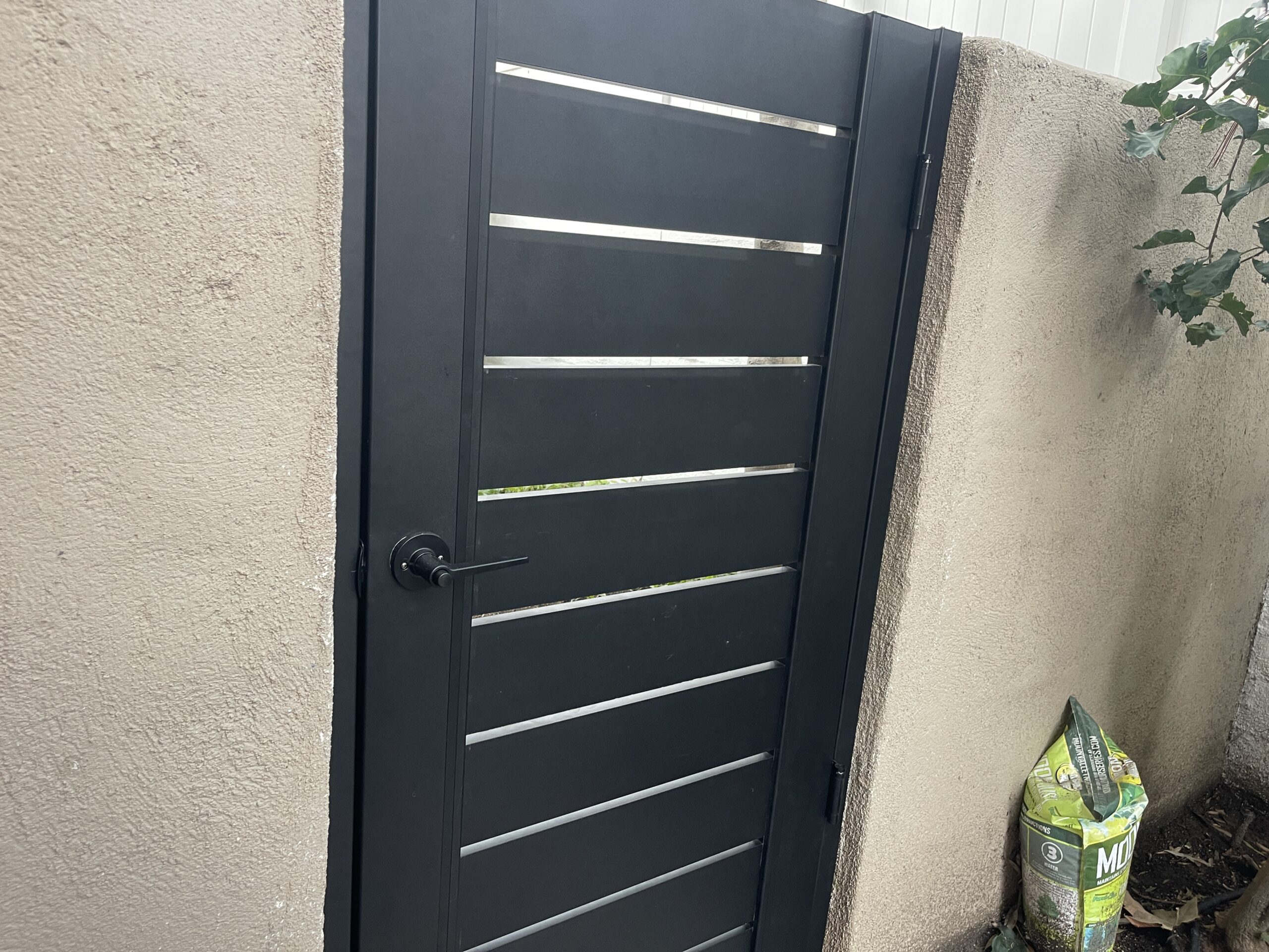 Modern aluminum gate installed next to a textured wall with a planter nearby.
