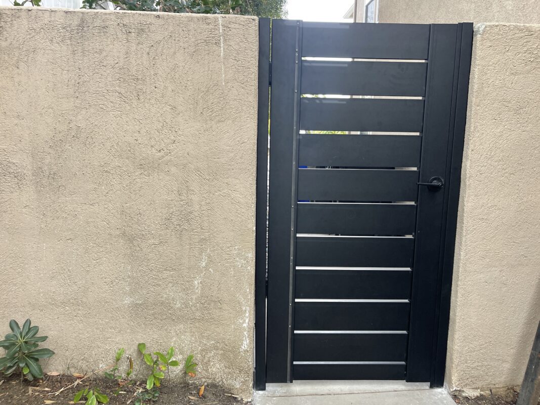 A modern black aluminum gate installed in a beige wall, enhancing property safety and style.