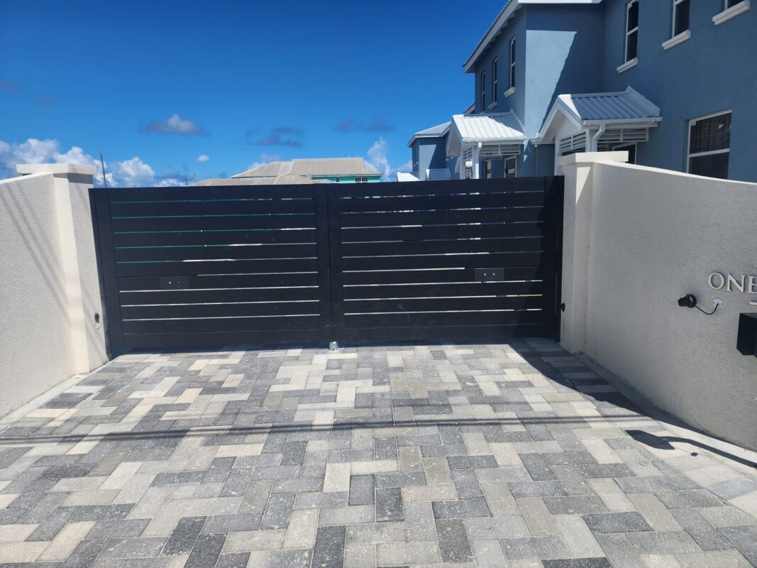 A modern black double swing gate with stone pavers in front of a residential property.