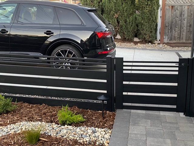 A sleek black aluminum fence and gate with a car parked behind it in a residential setting.