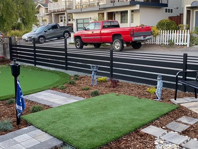 Black aluminum fence surrounds green lawn with decorative statues and a red truck parked nearby.