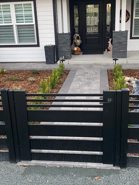 Sleek black aluminum gate leading to a paved walkway in a landscaped front yard.