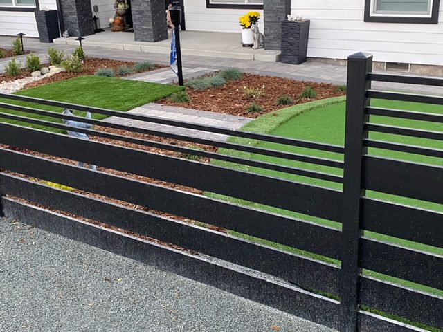 A sleek black aluminum fence and gate in a residential landscape design.