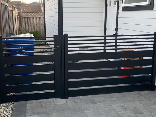 Modern black aluminum fence and gate design installed in a residential yard.