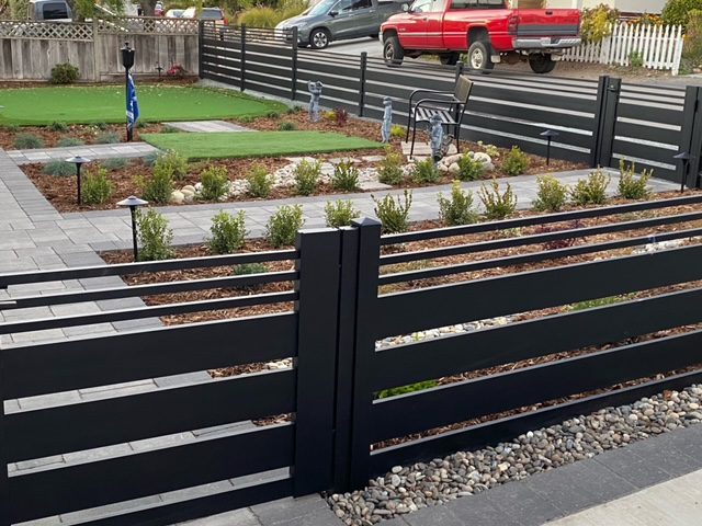 Installed black aluminum fence surrounding a landscaped yard with plants and decorative stones.