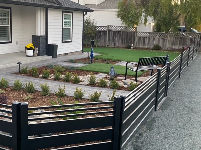 Sleek black aluminum fence surrounding landscaped yard with flowers and seating area.