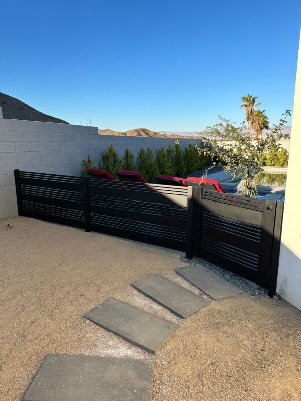 Matte black aluminum fence gate with horizontal slats in a desert landscape.